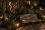 Banco de madera iluminado de noche en el jardín de Finca Adalgisa, con una copa de vino y un libro