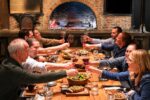 Argentine asado toast around the long table, fire burning in the background, at Finca Adalgisa