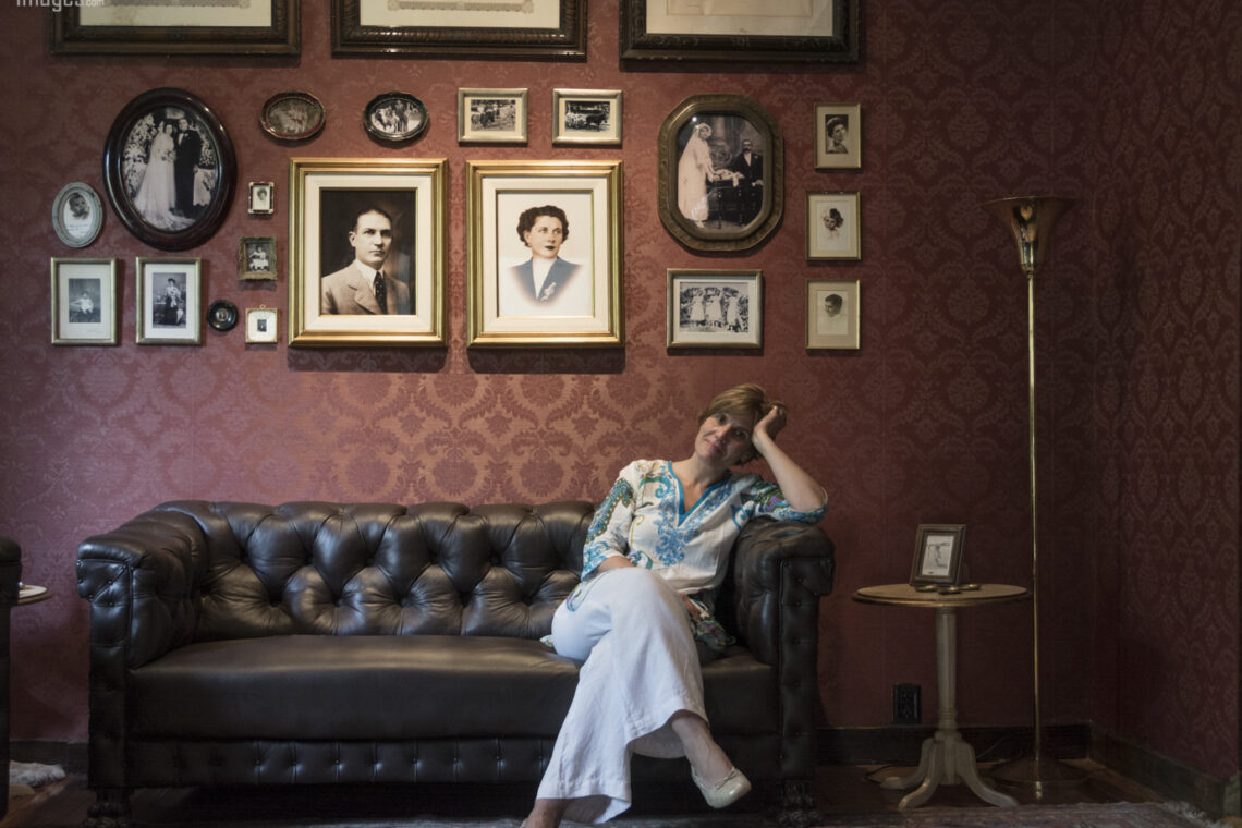 Una mujer sola en un salón antiguo. El cuerpo en movimiento, casi suspendido, como si escuchara una música que no se oye. Detrás, una pared cubierta de retratos: miradas del pasado que observan, acompañan, sostienen.