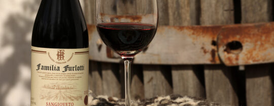 Empanadas caseras servidas en un plato junto a una botella y una copa de vino, sobre una mesa al aire libre, evocando rituales heredados, encuentro y continuidad entre generaciones.