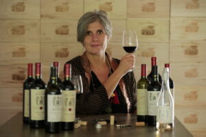 Gabriela Furlotti sosteniendo una copa de vino junto a botellas en la bodega.